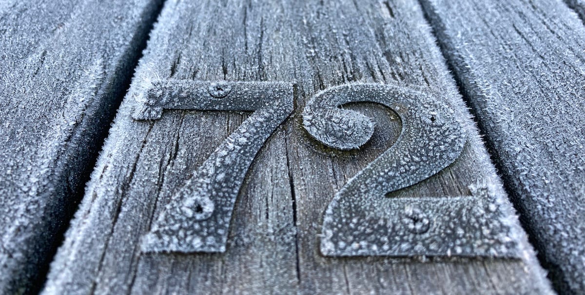 Two metal numbers, 7 and 2, as you might find on a door marking the house number, but they're fixed to a table because it used to be in a pub garden. The table and numbers are covered in frost. 