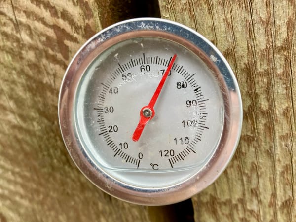 A compost thermometer poking between two planks of wood measuring 71 degrees centigrade.
